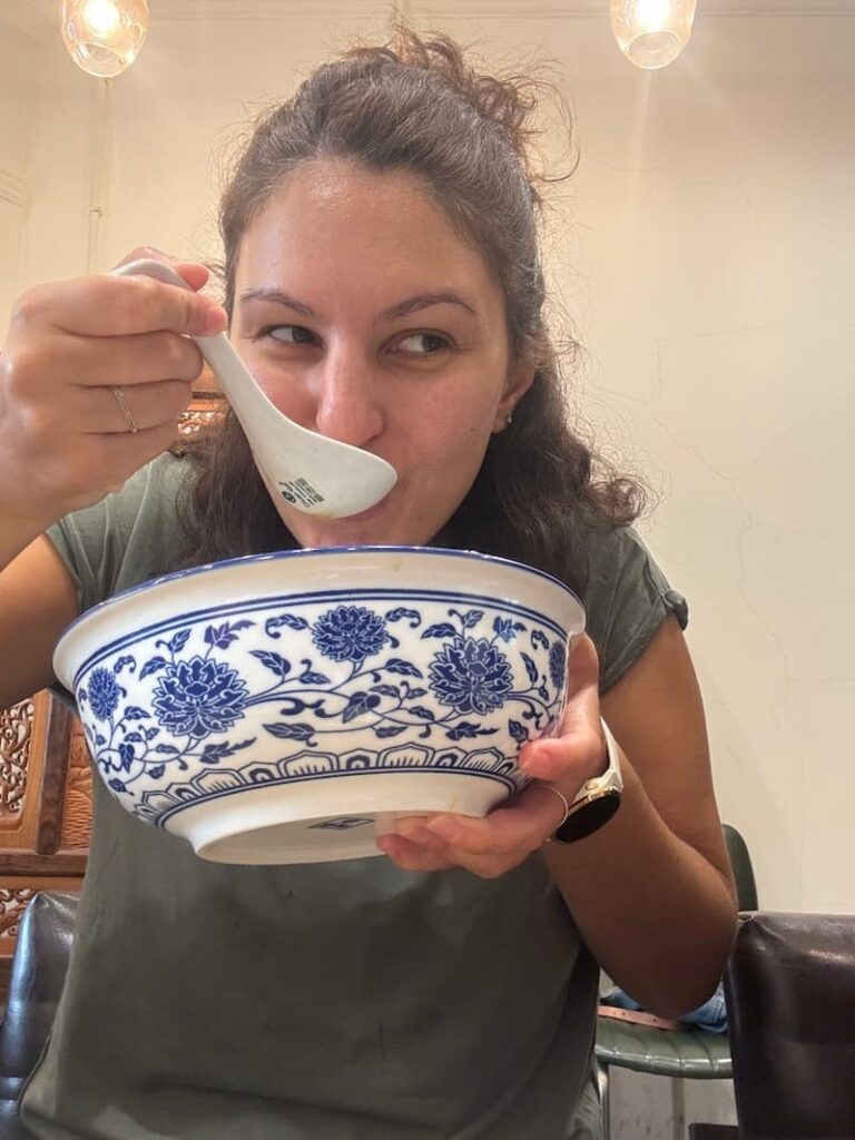 Woman enjoying a large bowl of traditional beef noodle soup at a local restaurant in Taipei.