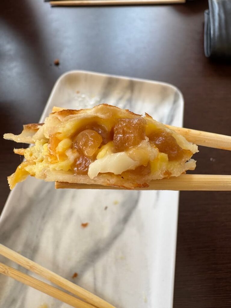 Close-up of a sliced Taiwanese egg crepe held by chopsticks, revealing a gooey filling of melted cheese and translucent boba pearls.
