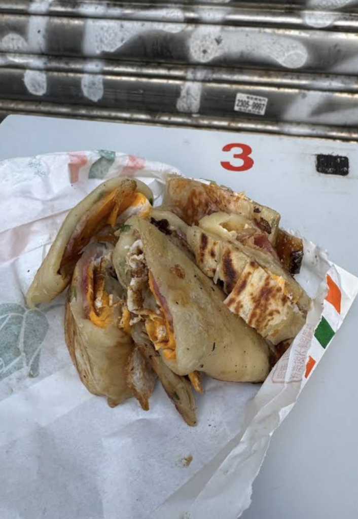 Sliced Taiwanese dan bing (egg pancake roll) wrapped in paper, filled with egg and savory ingredients, served at a breakfast spot in Taipei.
