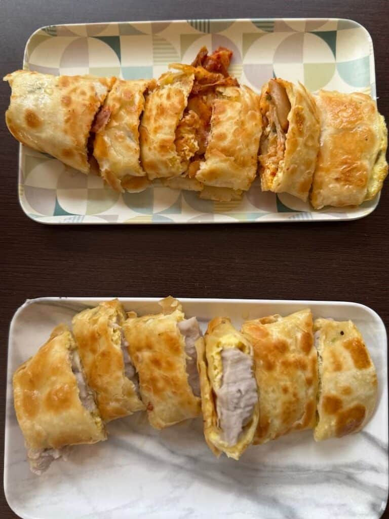 Two rectangular plates showcasing sliced Taiwanese egg crepes (danbing), with one variation filled with savory kimchi and another stuffed with smooth taro paste.