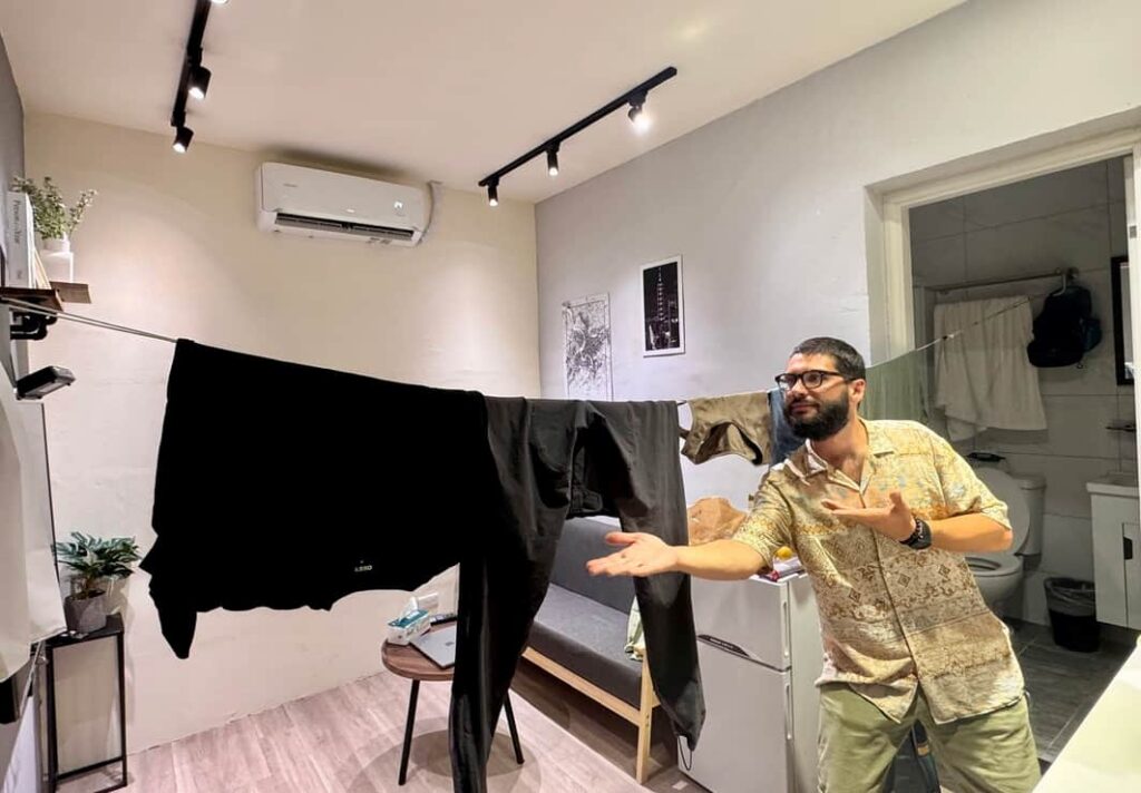 A traveler gesturing toward clothes hanging on an indoor drying line in a Taipei apartment.