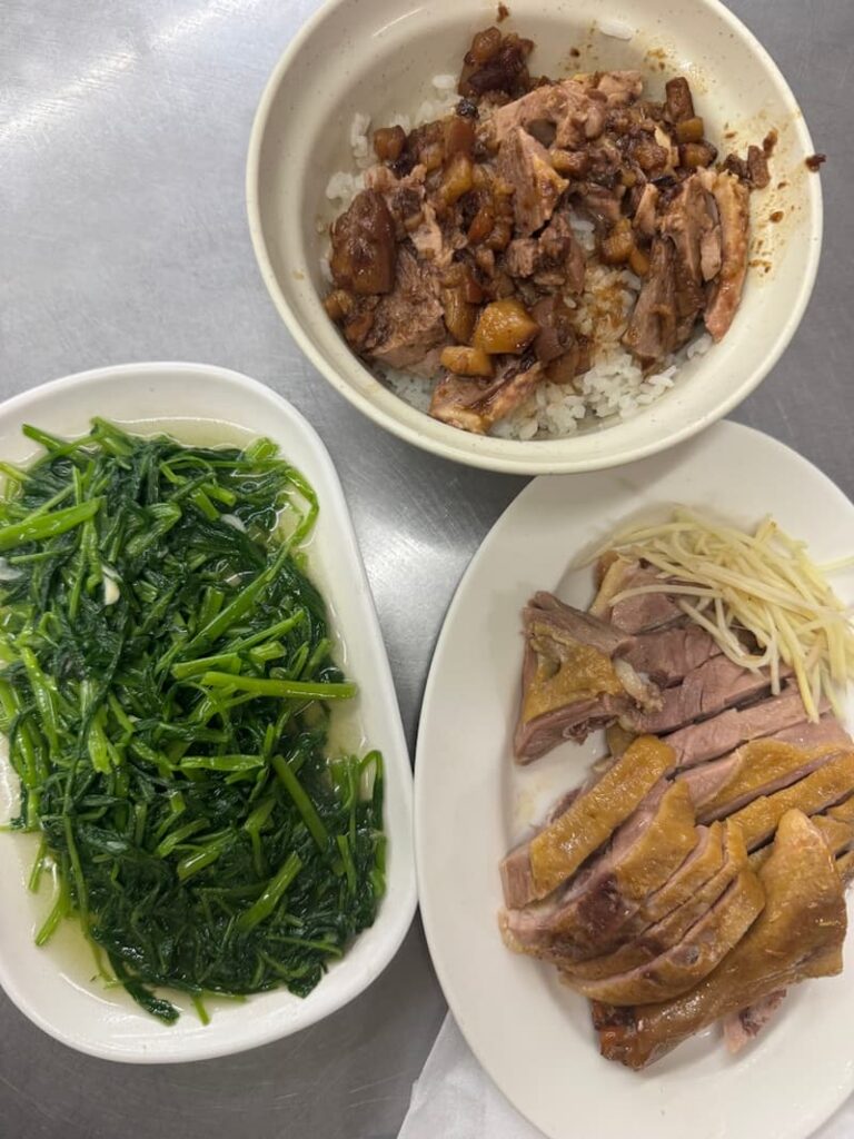 A traditional Taiwanese spread featuring a bowl of braised pork rice, a plate of sliced savory duck meat garnished with ginger strips, and a side of vibrant green water spinach.