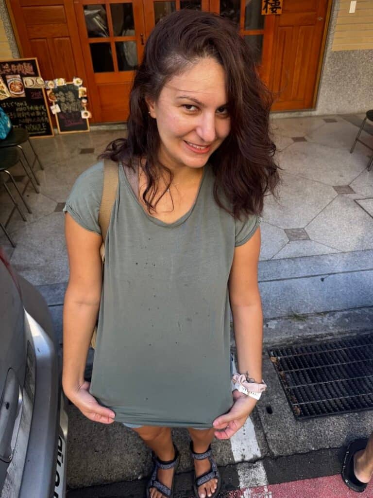 The travel blogger smiling while showing off small food splashes on her shirt after a messy dining experience with beef noodle soup in Taipei.