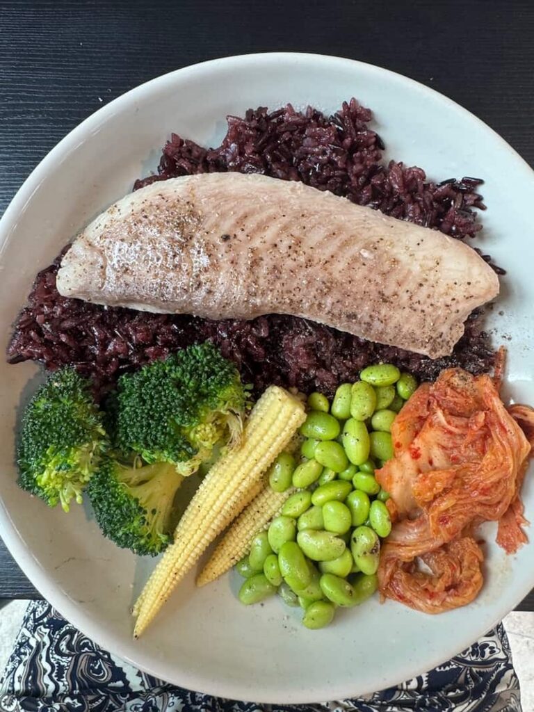 Healthy high-protein meal bowl in Taipei featuring fish, black rice, broccoli, baby corn, edamame, and kimchi.