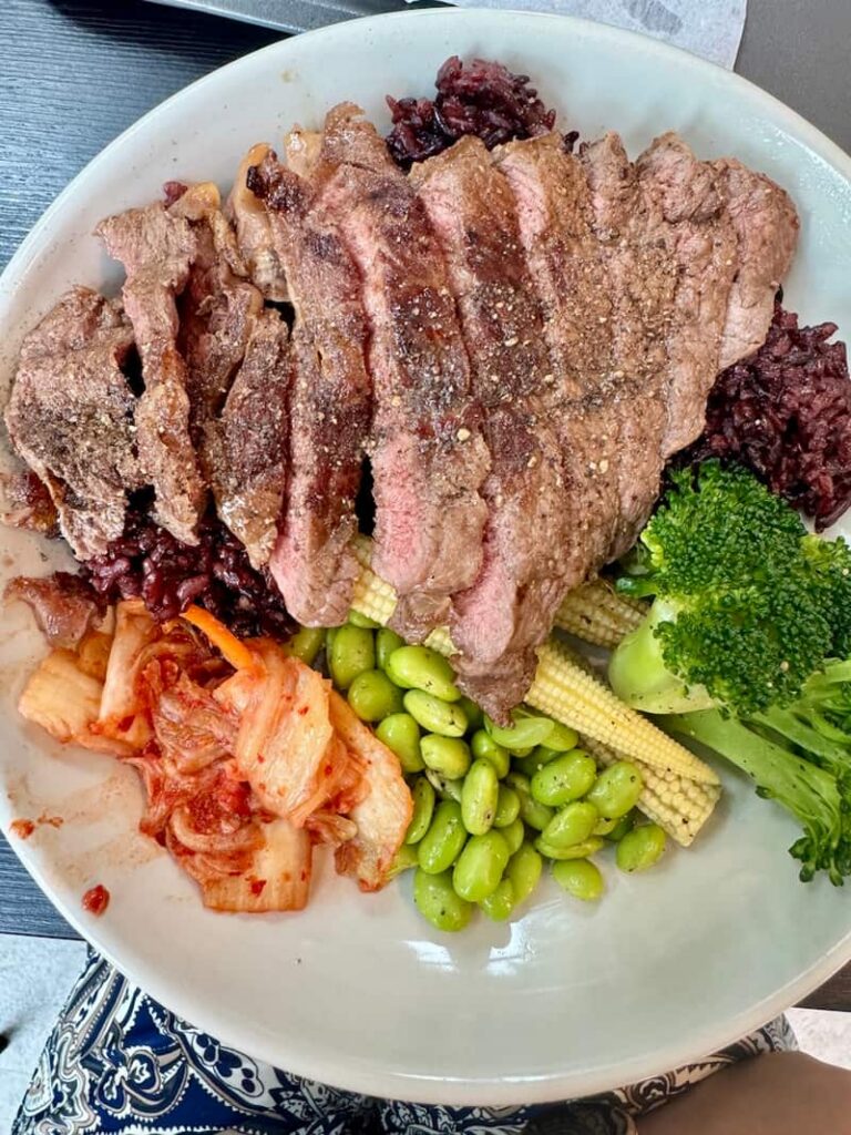 Balanced fitness meal with sliced steak, black rice, edamame, broccoli, baby corn, and kimchi at a healthy restaurant in Taipei.