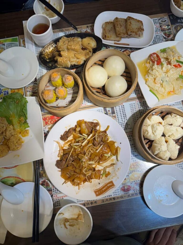 A top-down view of a table spread with a variety of Hong Kong-style dim sum dishes at a restaurant in Taipei, including steamed buns, dumplings, rice noodle rolls, and pan-fried turnip cake, as featured in our guide about the best places to eat in Taipei.