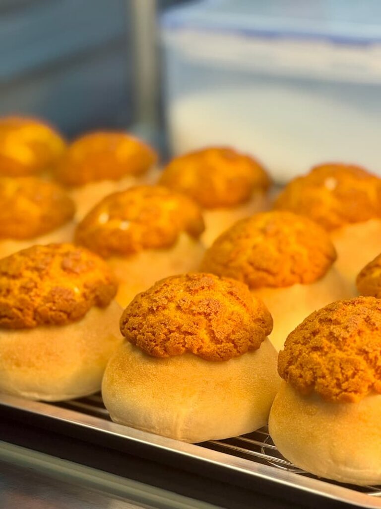 Freshly baked buns with smooth dough bases and golden, cracked crusts arranged on a metal display tray.