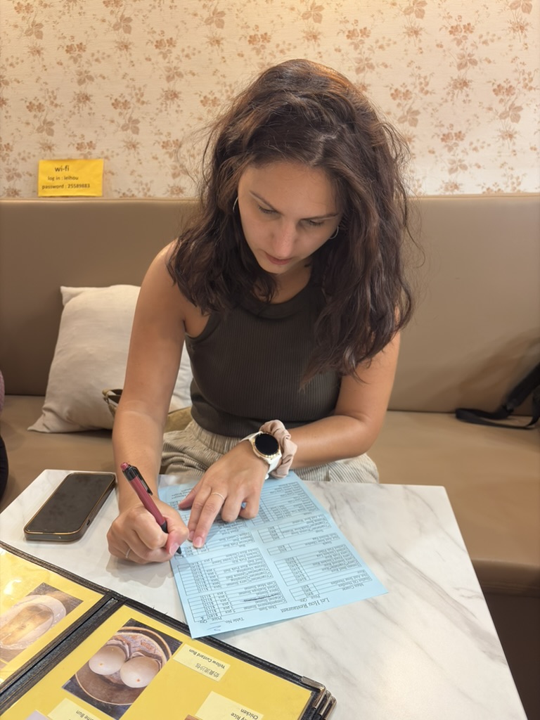 The main blogger of this travel blog, seated at a restaurant table and using a red pen to fill out a blue order slip at a local restaurant in Taipei.
