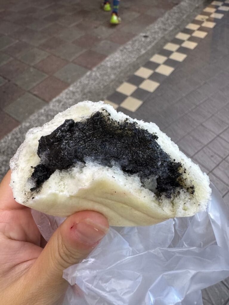 A fluffy white steamed bun pulled apart to show a rich, gooey black sesame paste filling.