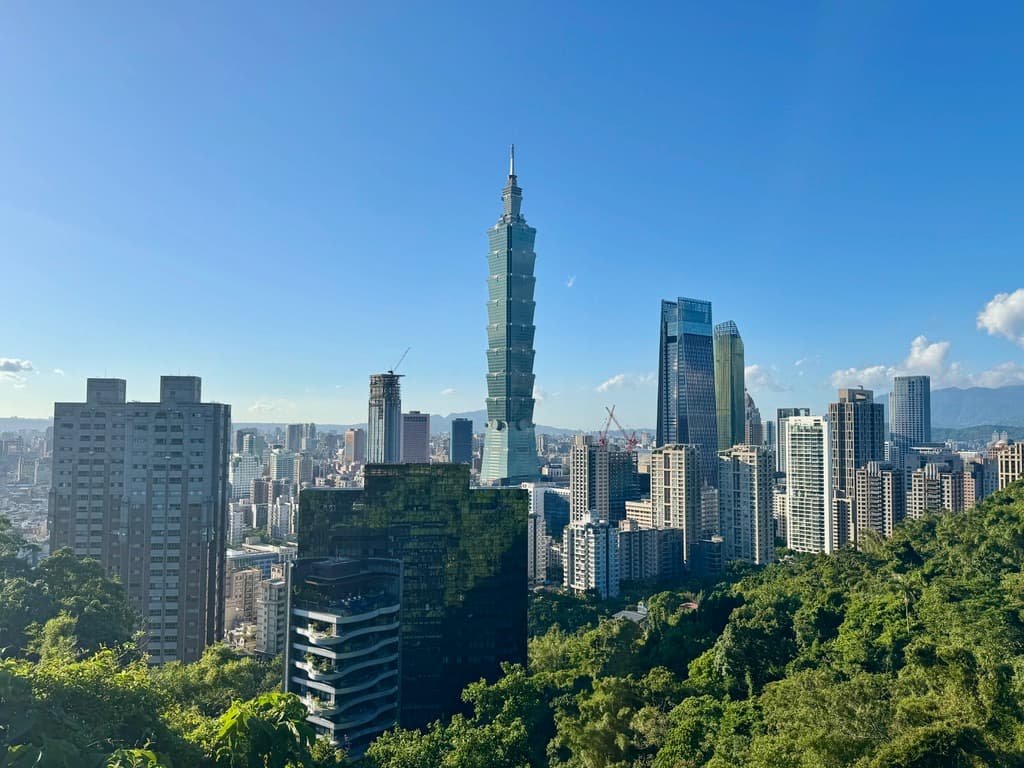 Panoramic view of the Taipei skyline featuring the iconic Taipei 101 skyscraper under a clear blue sky, viewed from Elephant Mountain.