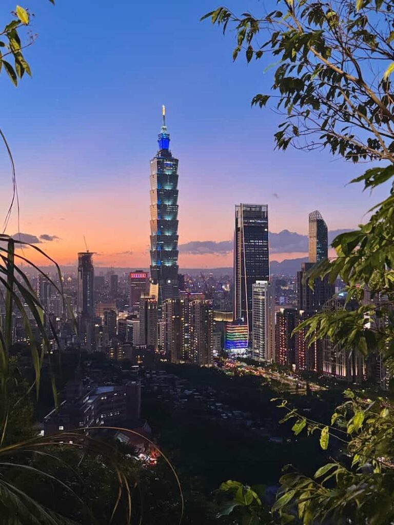 View of the Taipei 101 skyscraper framed by tree branches during a colorful sunset from Elephant Mountain, as featured in our guide answering 'is elephant mountain worth it?'