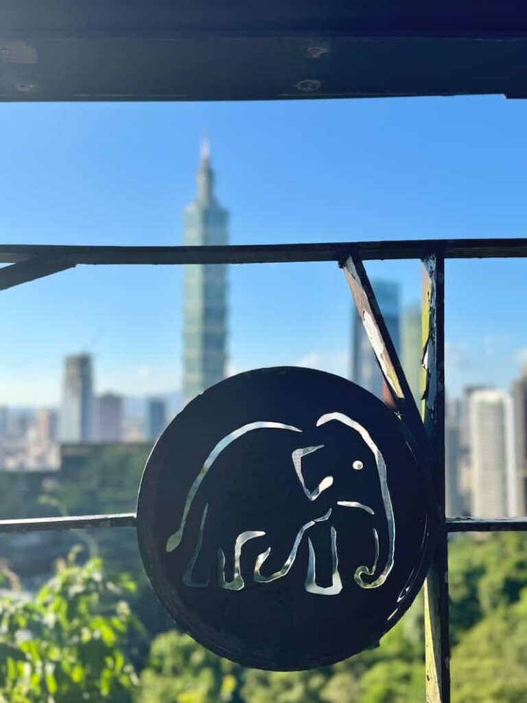 Decorative metal cutout sign with an elephant motif against the backdrop of the Taipei skyline and Taipei 101, as featured in our guide answering 'is elephant mountain worth it?'