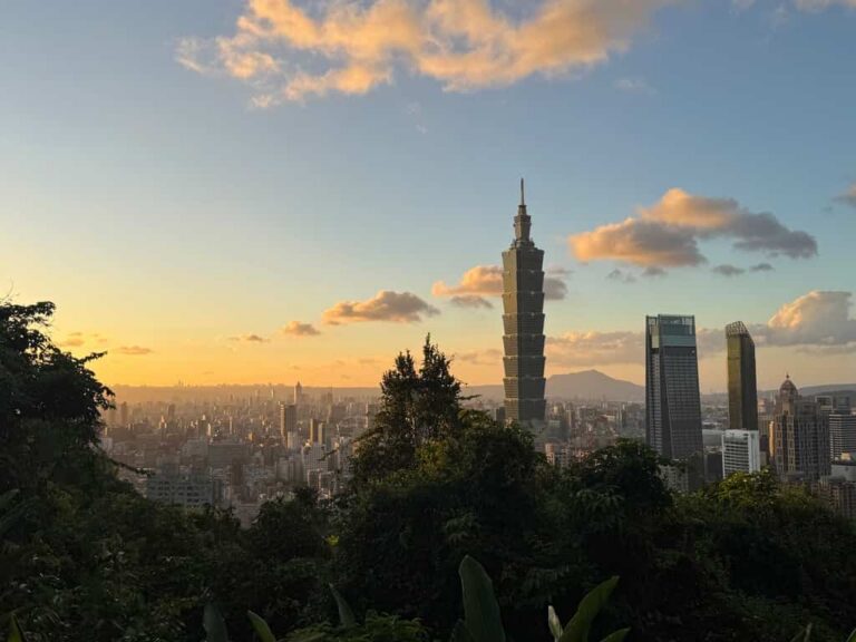 Panoramic sunset view over the Taipei city skyline and Taipei 101 tower from a high vantage point.