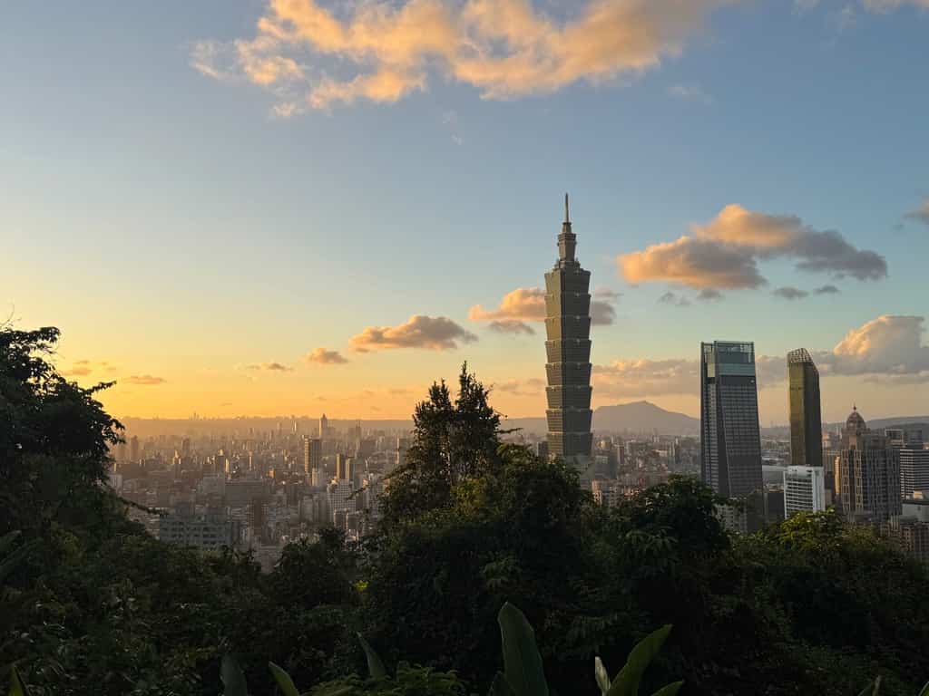Panoramic sunset view over the Taipei city skyline and Taipei 101 tower from a high vantage point.
