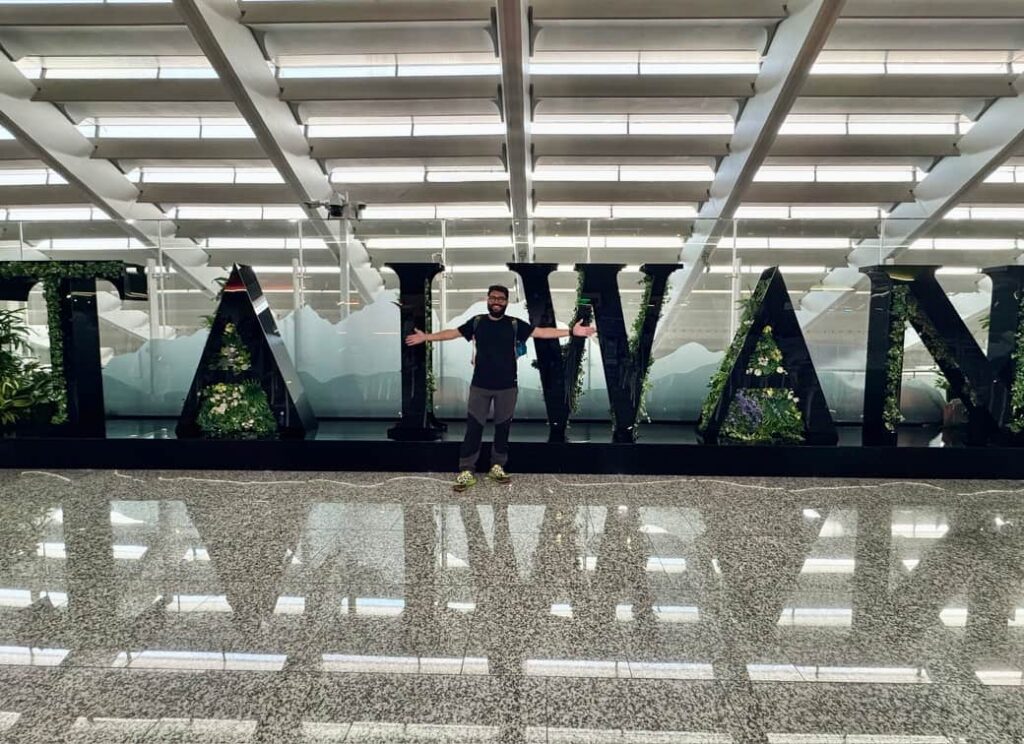 A traveler posing with open arms in front of a large decorative "TAIWAN" sign at the airport, as featured at the beginning of our 'Is Taipei worth visiting?' guide.