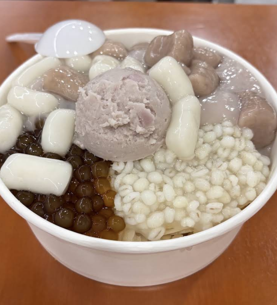 A white bowl filled with a traditional Taiwanese dessert featuring a central scoop of taro paste, topped with taro balls, chewy mochi pieces, brown pearls, and cooked barley, as featured in our guide about the best places to eat in Taipei. 